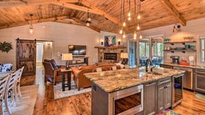 A spacious kitchen with a large island, wooden ceiling beams, and a stone fireplace.