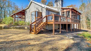 A wooden cabin with a stone foundation, a wooden deck, and a staircase leading to a covered porch.