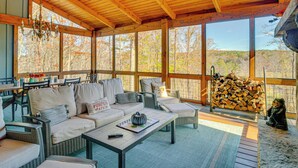A covered outdoor seating area with wicker furniture, a chandelier, and a view of the forest.