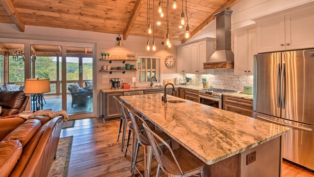 A spacious kitchen with a large island, stainless steel appliances, and a wooden ceiling.