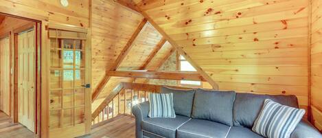 A wooden interior with a sofa, a patterned rug, and a wooden door.