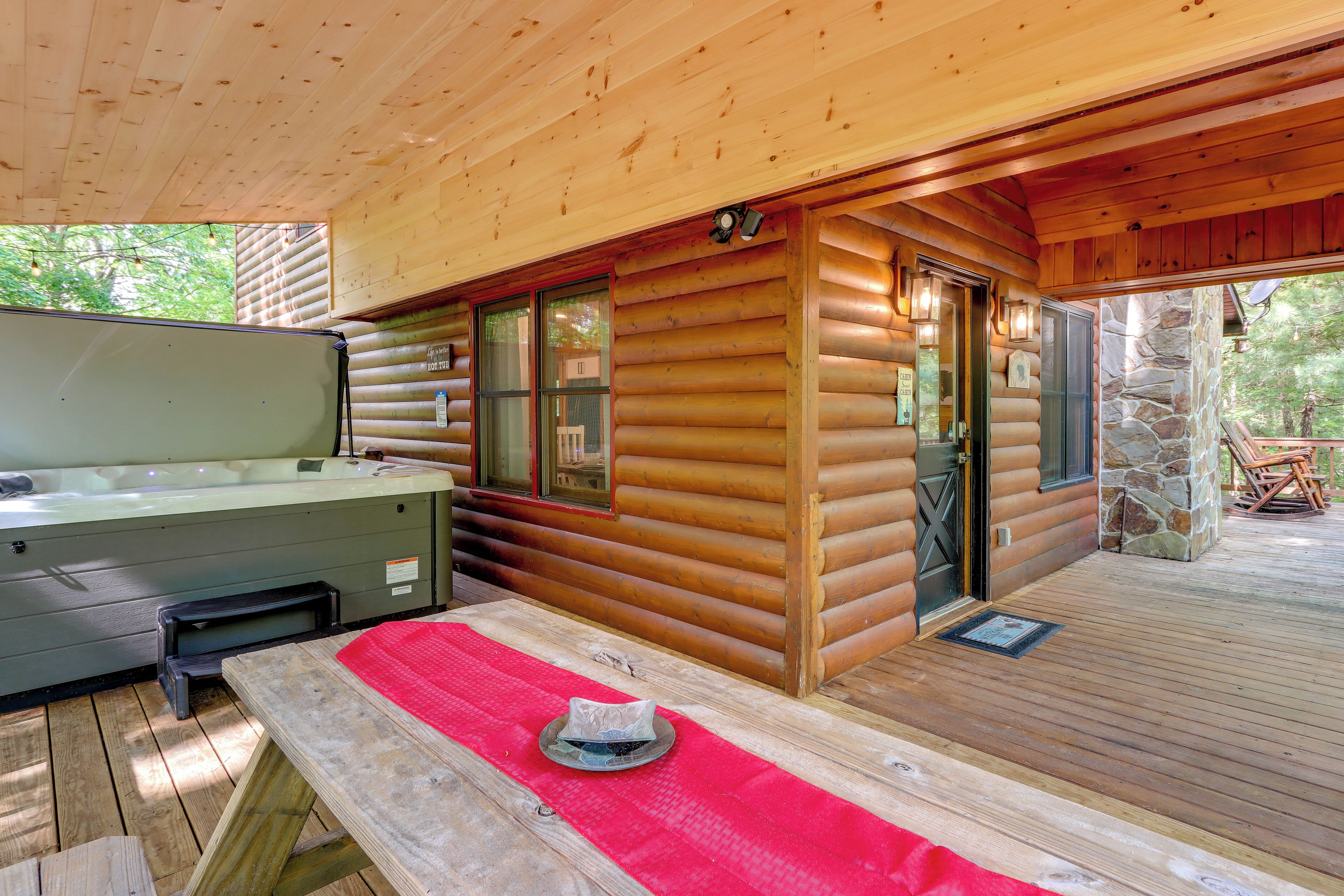 Een blokhut met een hottub, houten terras en een stenen muur.