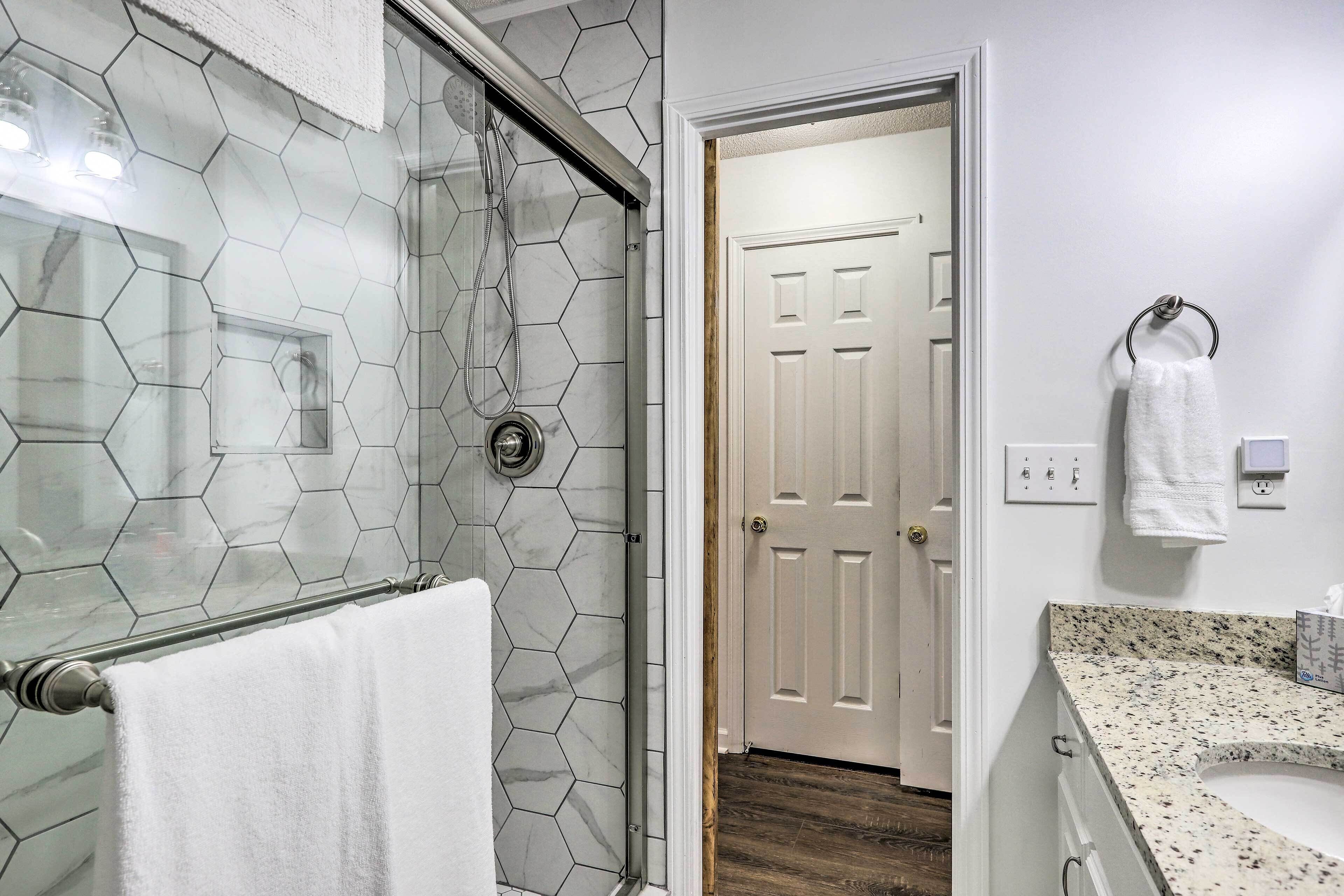 A bathroom with a shower, a white door, a towel rack, and a sink with a speckled countertop.