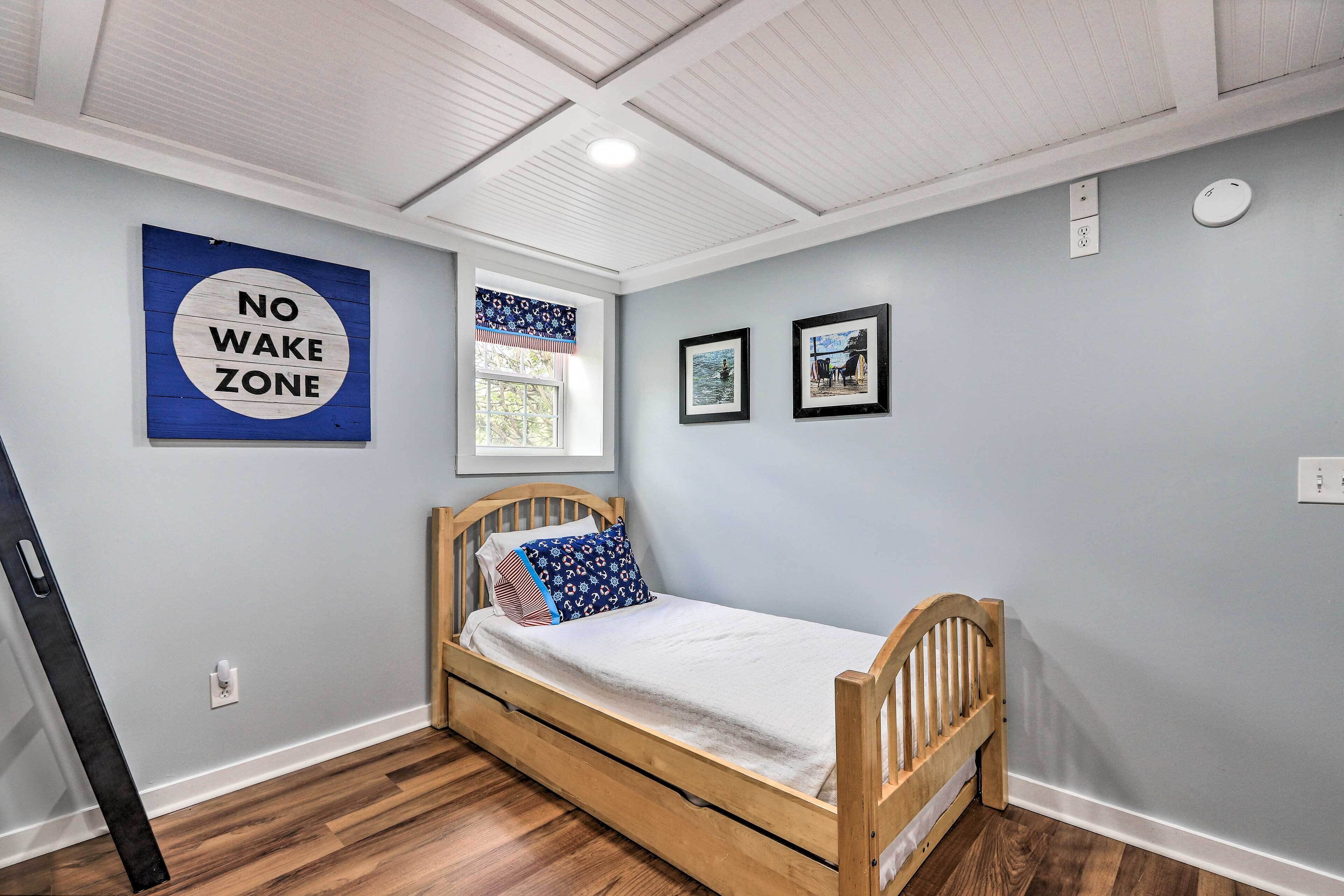 A bedroom with a wooden bed, a "NO WAKE ZONE" sign, a window with a view, and two framed pictures on the wall.