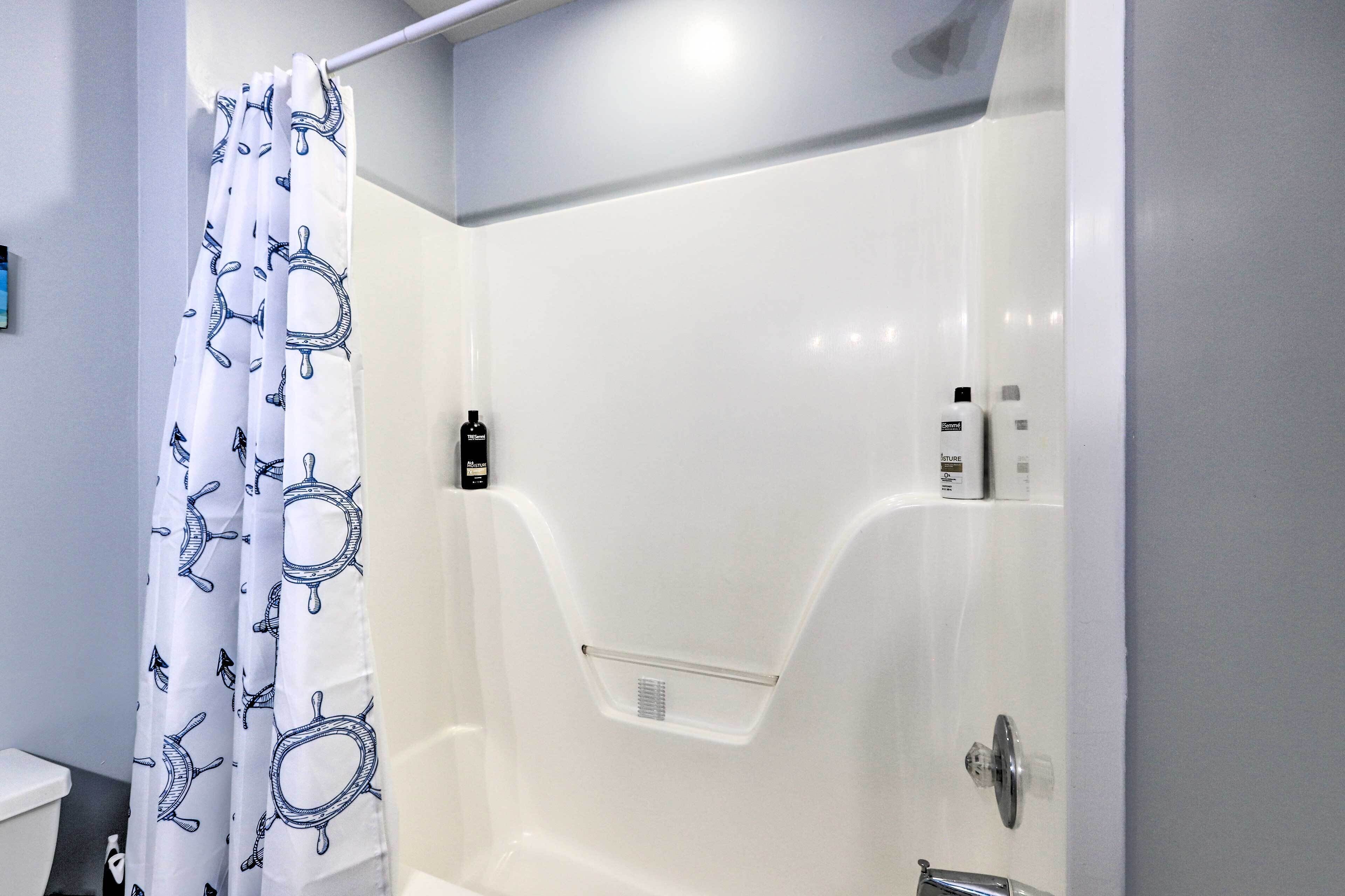 A bathroom with a white shower enclosure, a toilet, and a shower curtain with a nautical theme.