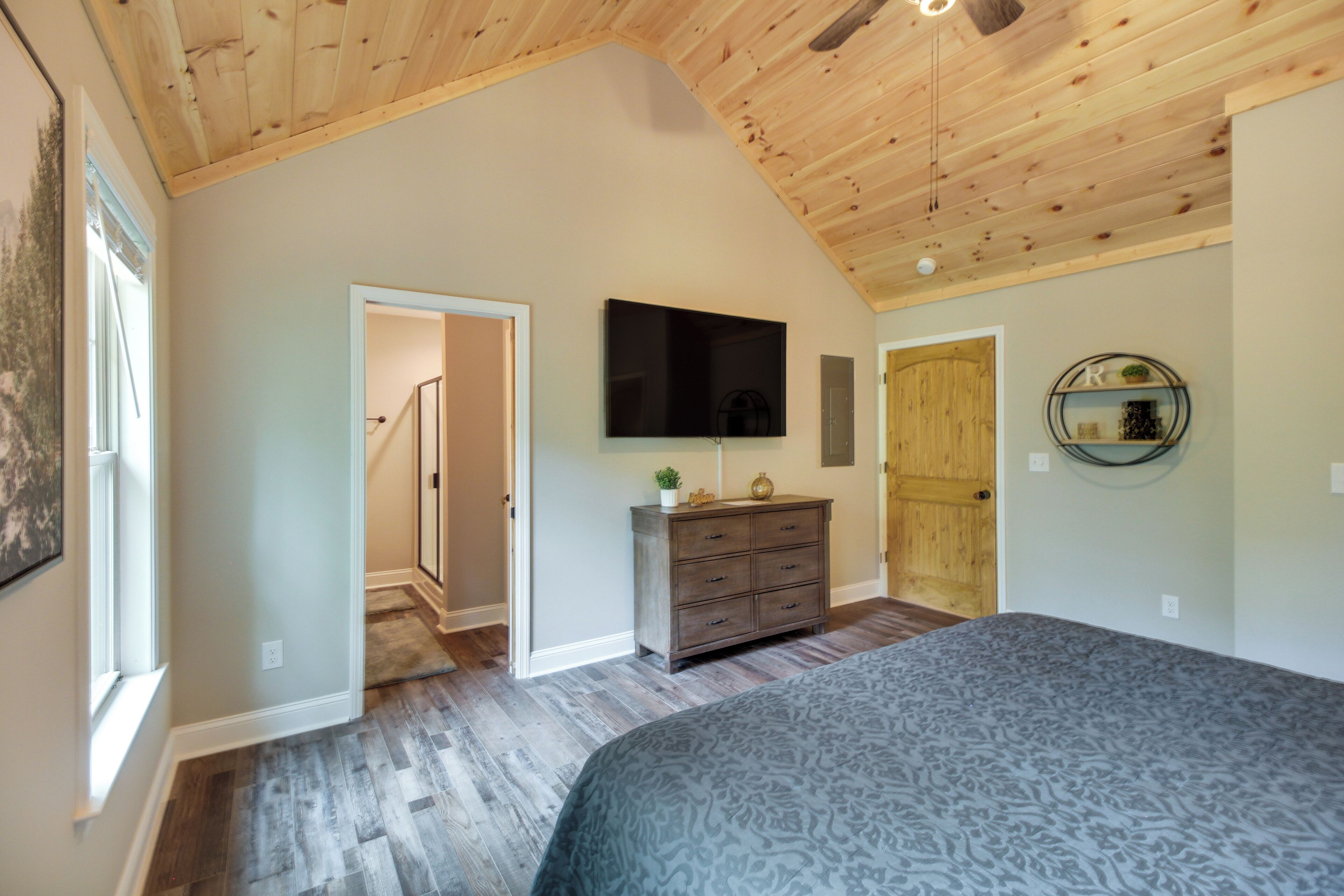 Een slaapkamer met een schuine plafond, een flatscreen televisie, een dressoir en een bed.