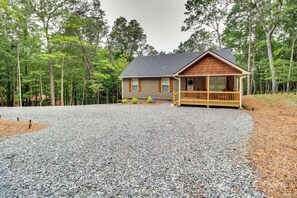 Une cabane avec une allée en gravier, une terrasse en bois et entourée d’arbres.