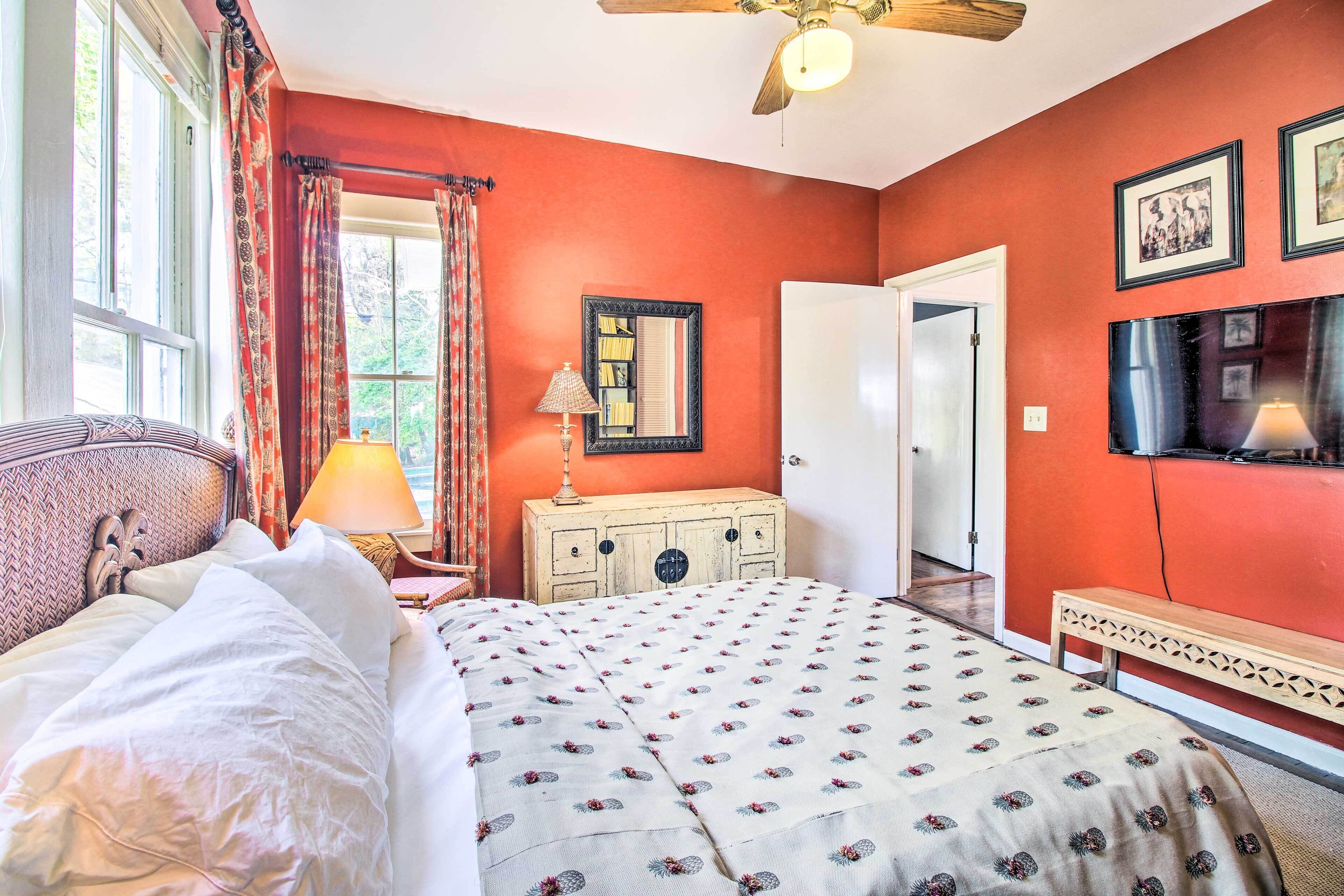 A bedroom with a bed, a nightstand, a dresser, a ceiling fan, and a television on the wall.