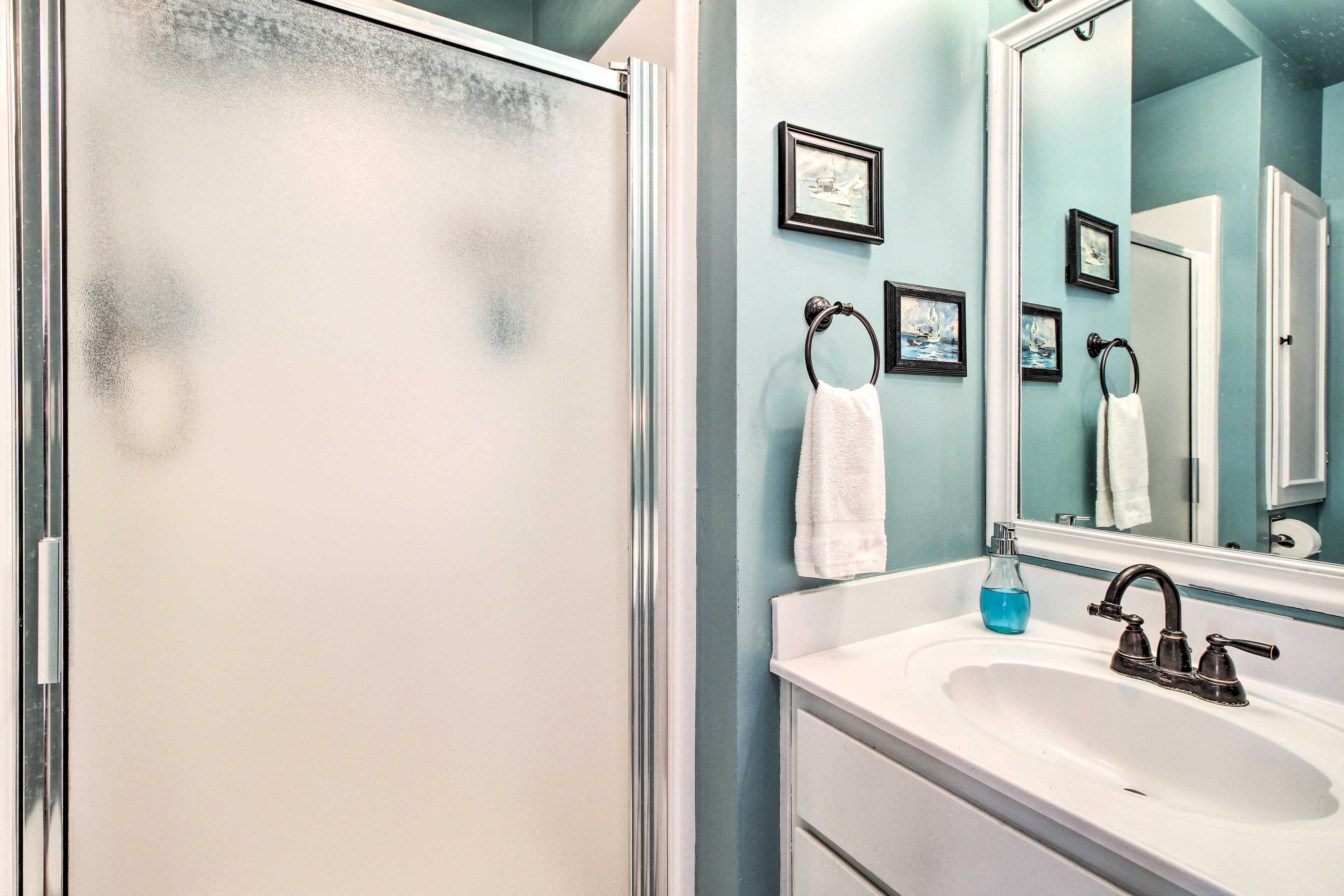 A bathroom with a glass shower door, a white sink with a black faucet, and a mirror with framed pictures on the wall.