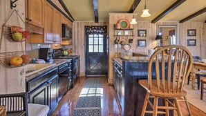 A rustic kitchen with wooden cabinets, a black stove, and a wooden chair.