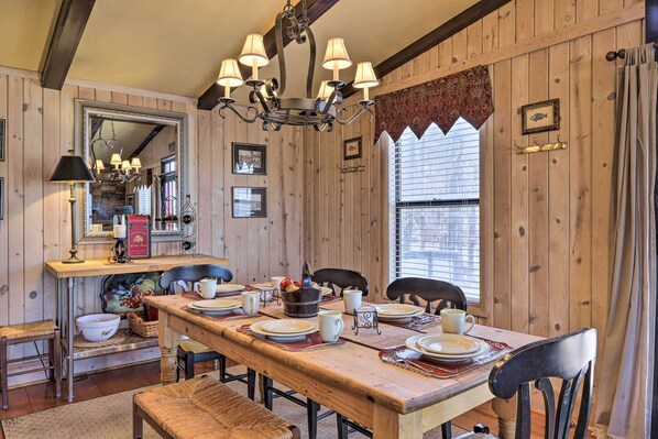 A wooden dining room with a long table set for four, surrounded by chairs. A chandelier hangs above, and a mirror is mounted on the wall. - Cozy Caymus Cabin ~ 3 Mi to Callaway Gardens! (Pine Mountain)