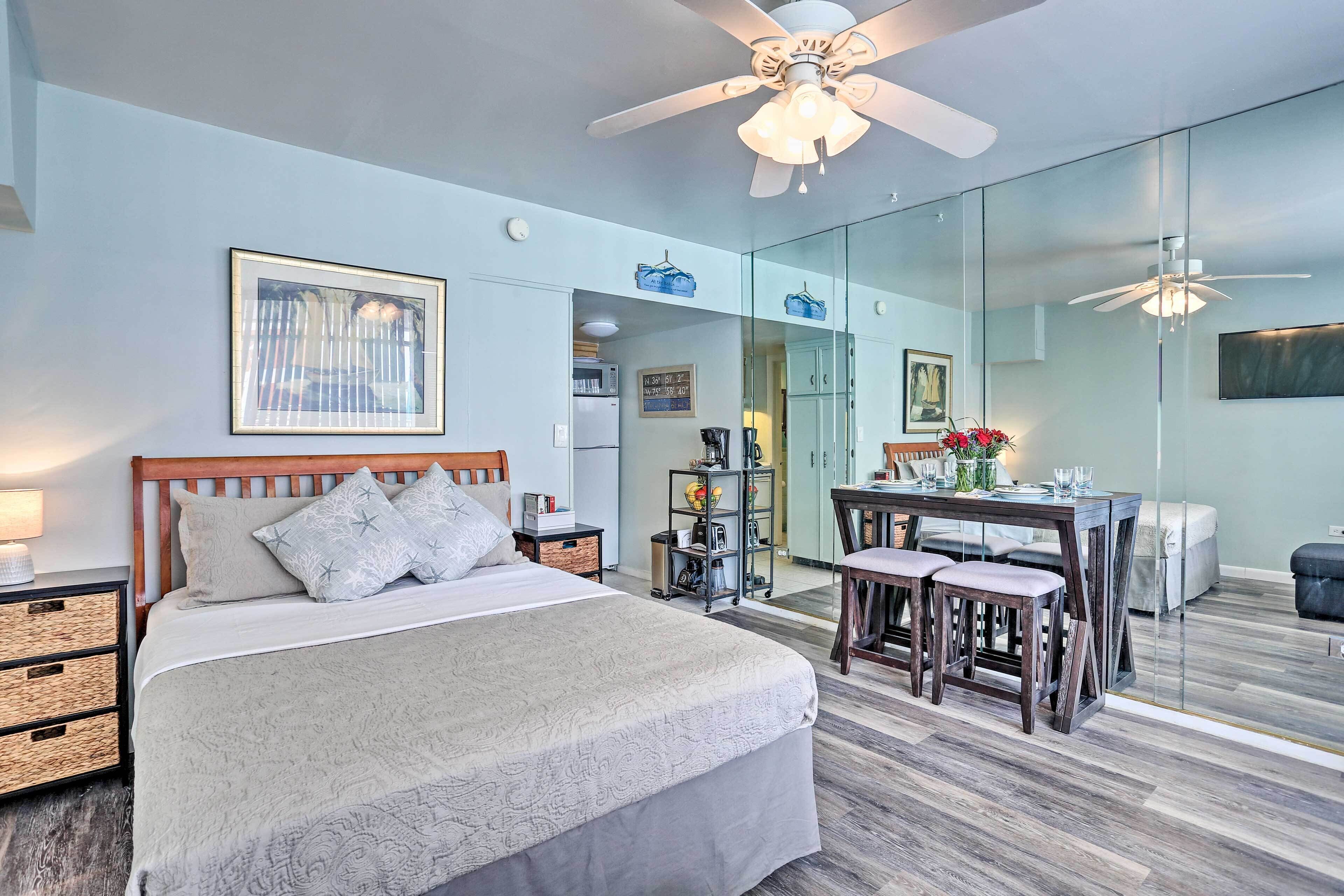 A bedroom with a bed, bedside tables, a desk with chairs, a mirror, and a ceiling fan.