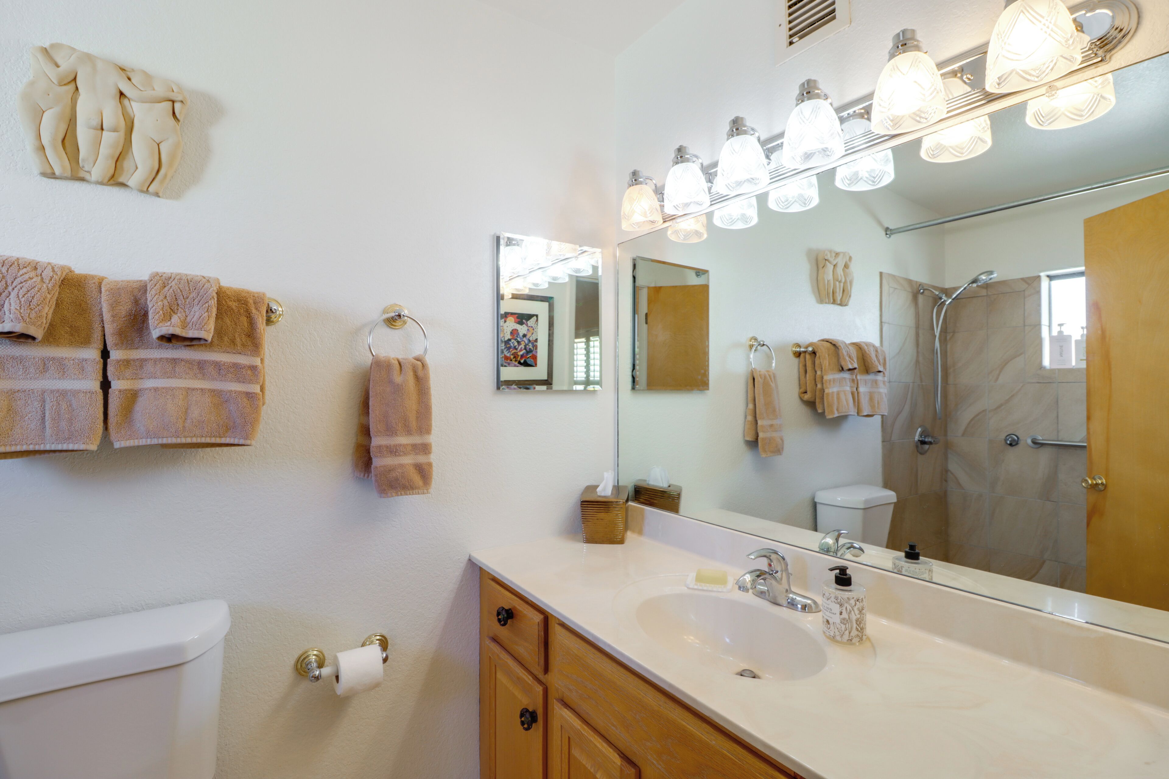 A bathroom with a large mirror, a sink, a toilet, and towels on the wall.