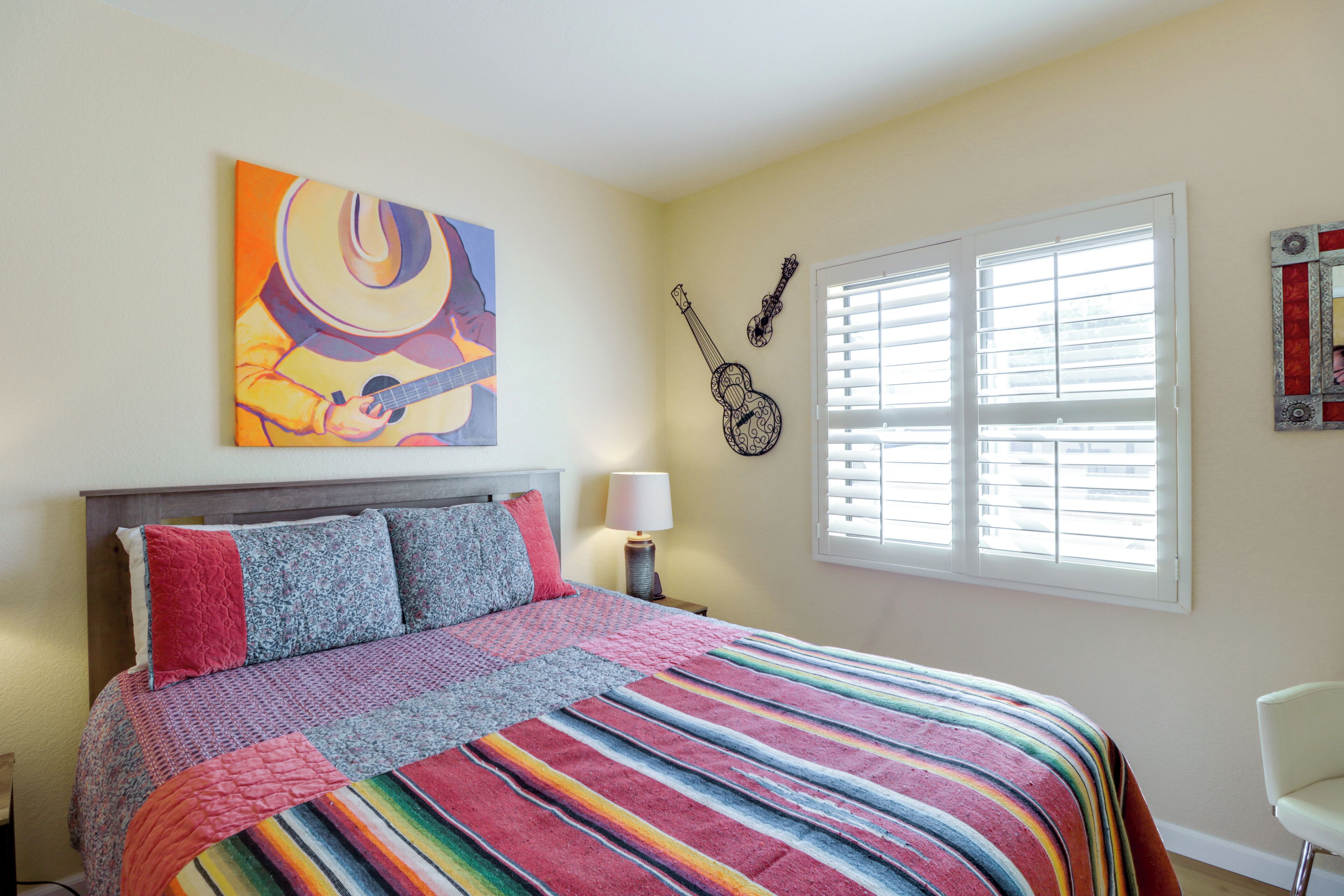 A bedroom with a bed, a window with blinds, a guitar, and a painting on the wall.