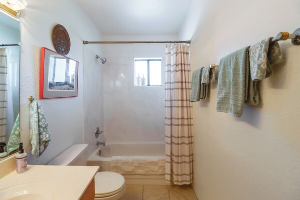 Een badkamer met een bad, toilet, douchegordijn en handdoeken aan de muur.
