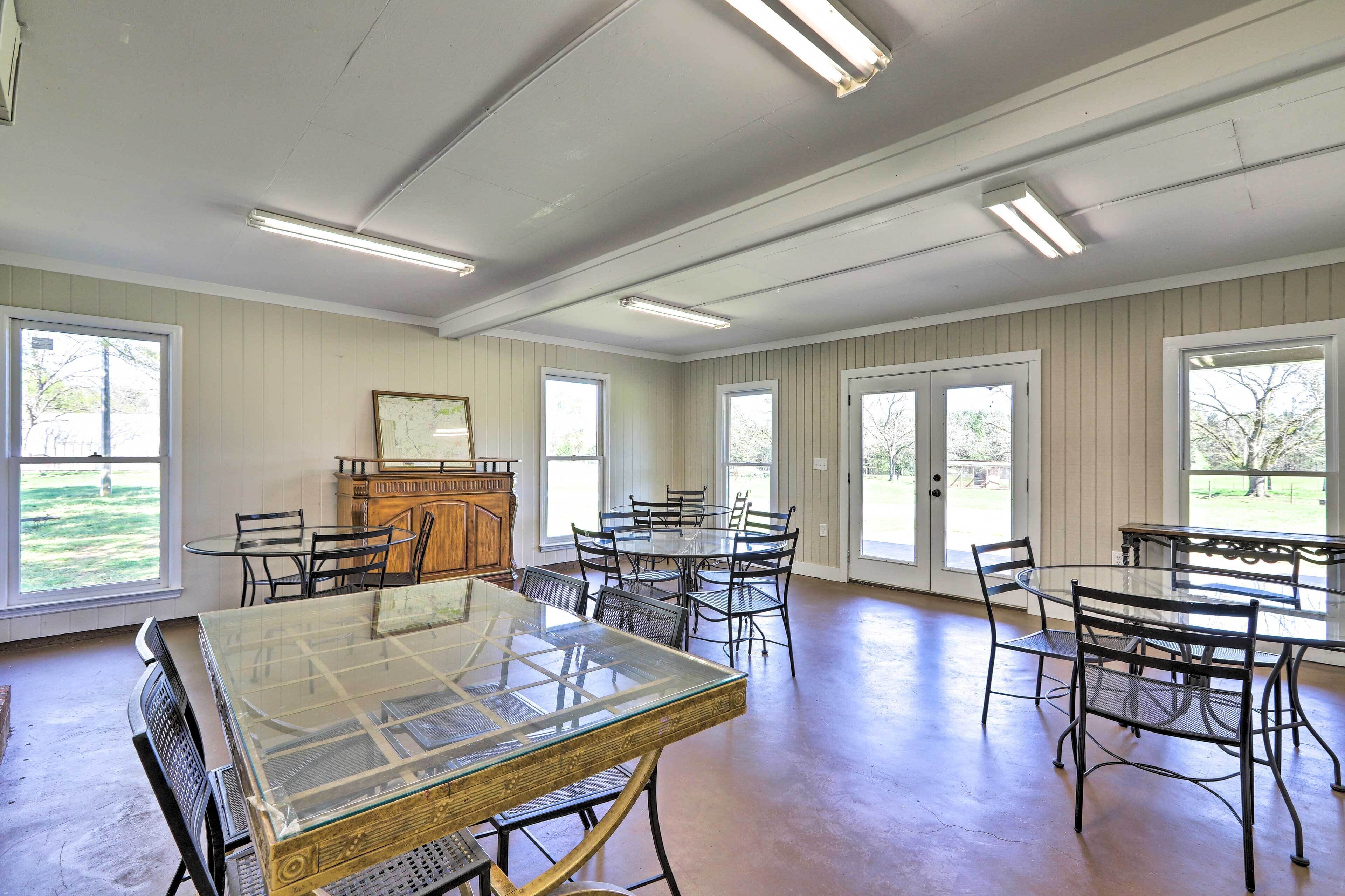 Une pièce spacieuse avec une table à plateau de verre entourée de chaises, un meuble en bois et de grandes fenêtres laissant entrer la lumière naturelle.