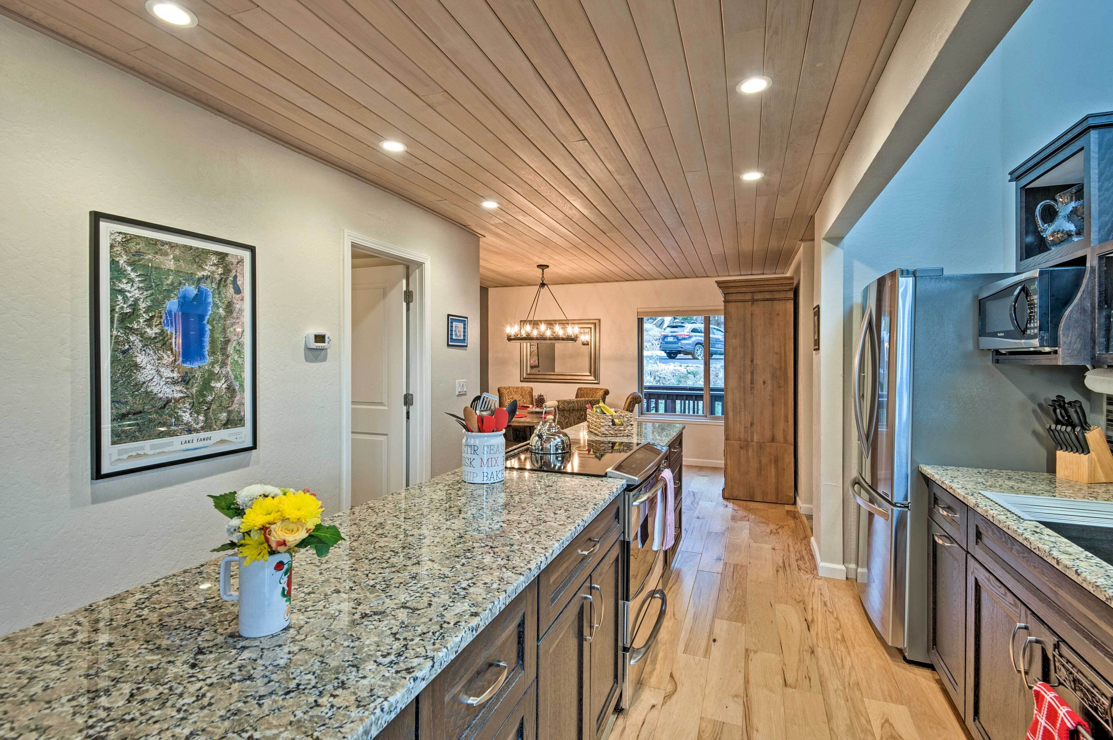 A kitchen with granite countertops, wooden cabinets, stainless steel appliances, and a hanging light fixture.