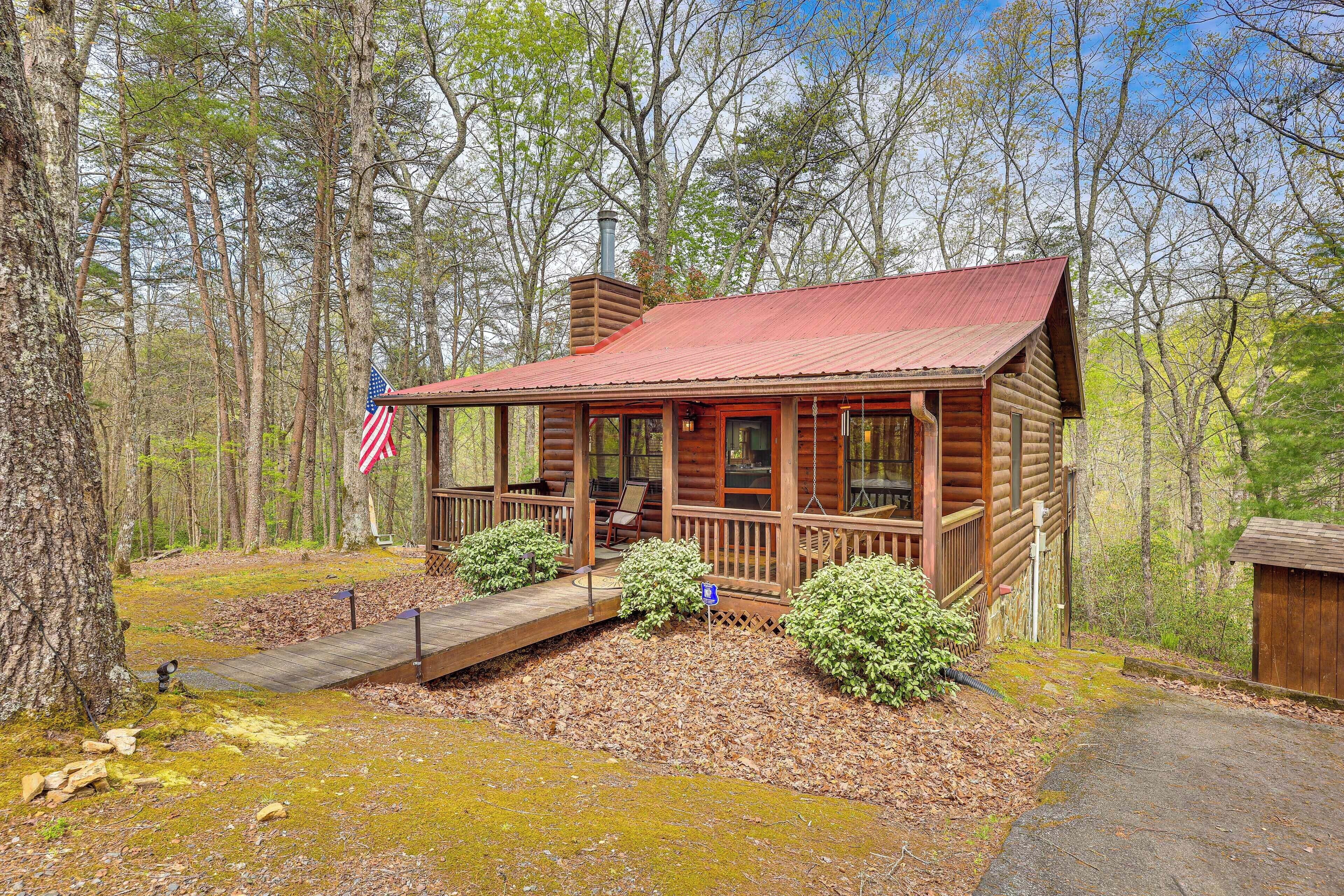 A rustic cabin with a porch, a chimney, and an American flag.
