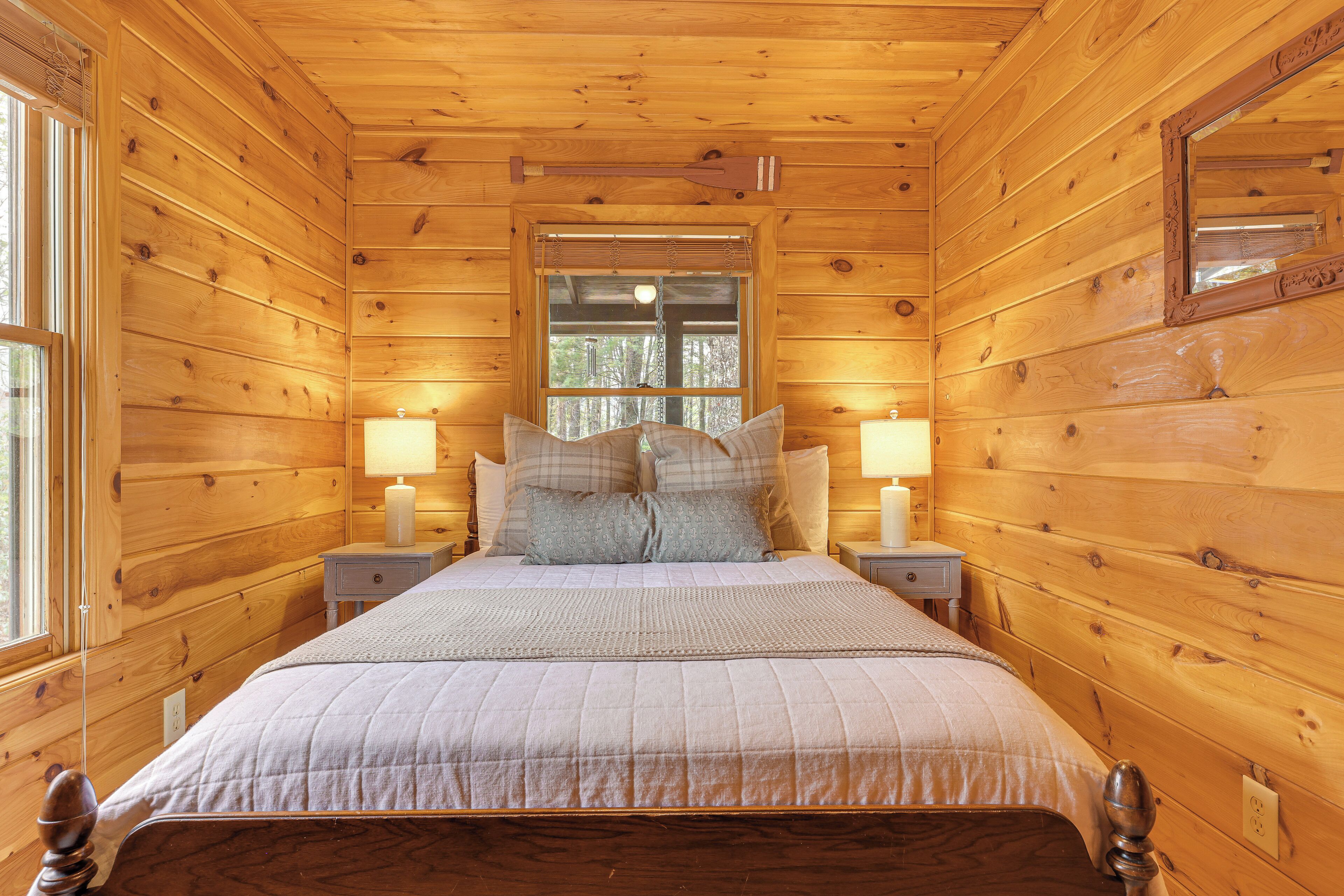 A wooden cabin bedroom with a bed, two bedside tables, and a window.