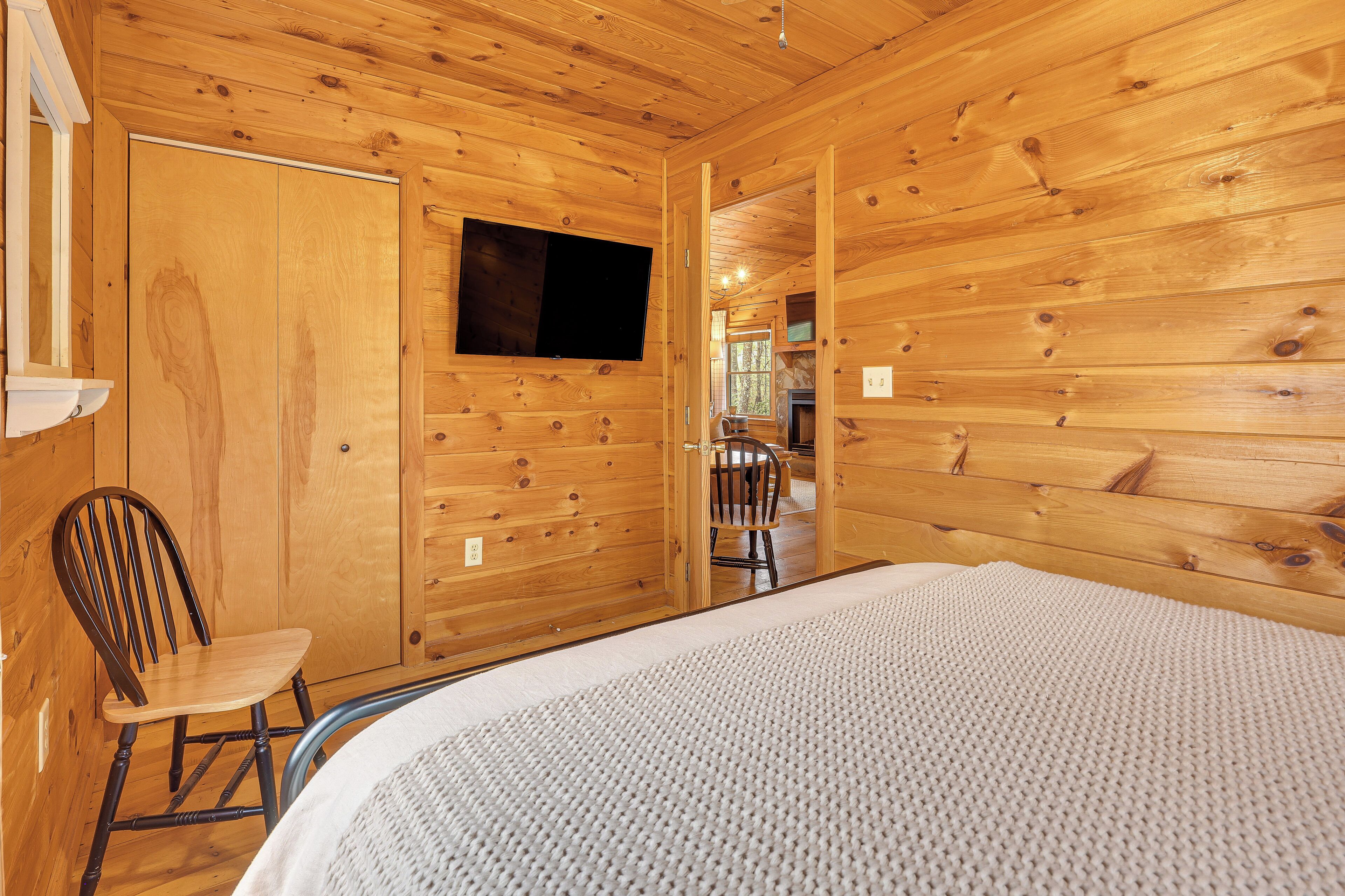 A wooden cabin interior with a bed, a chair, and a TV mounted on the wall.