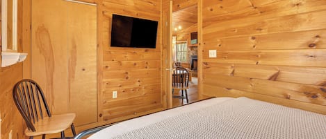 A wooden cabin interior with a bed, a chair, and a TV mounted on the wall.
