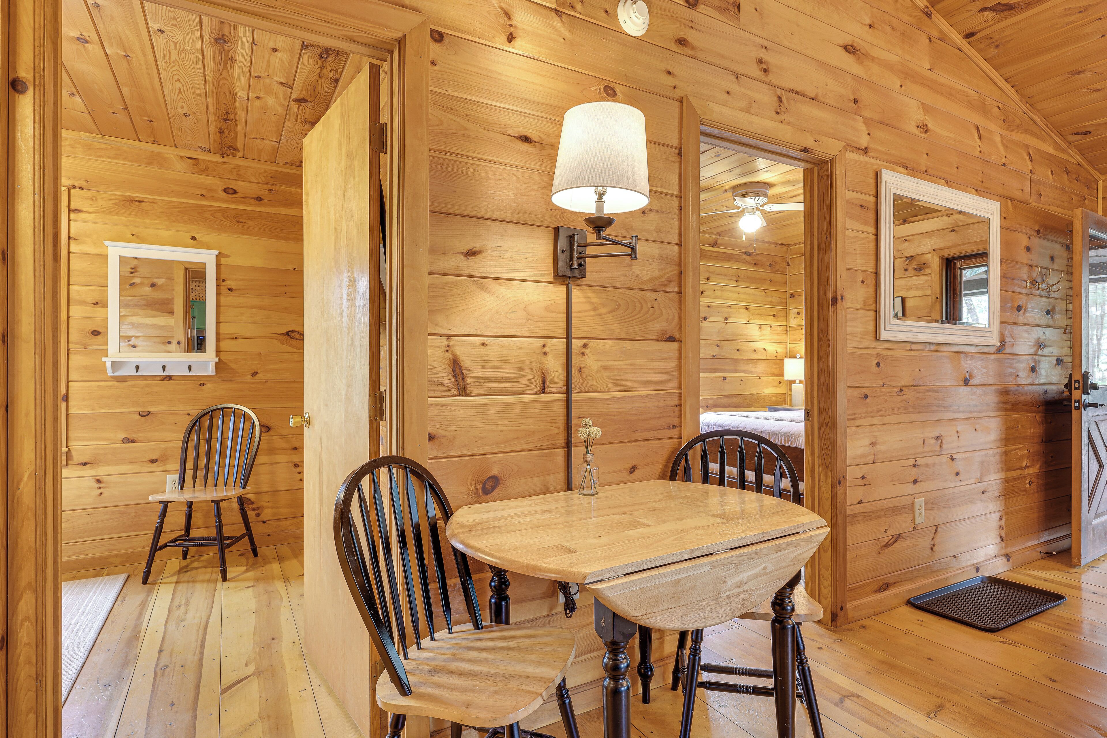 A wooden interior with a round wooden table, two chairs, a floor lamp, and a mirror on the wall.