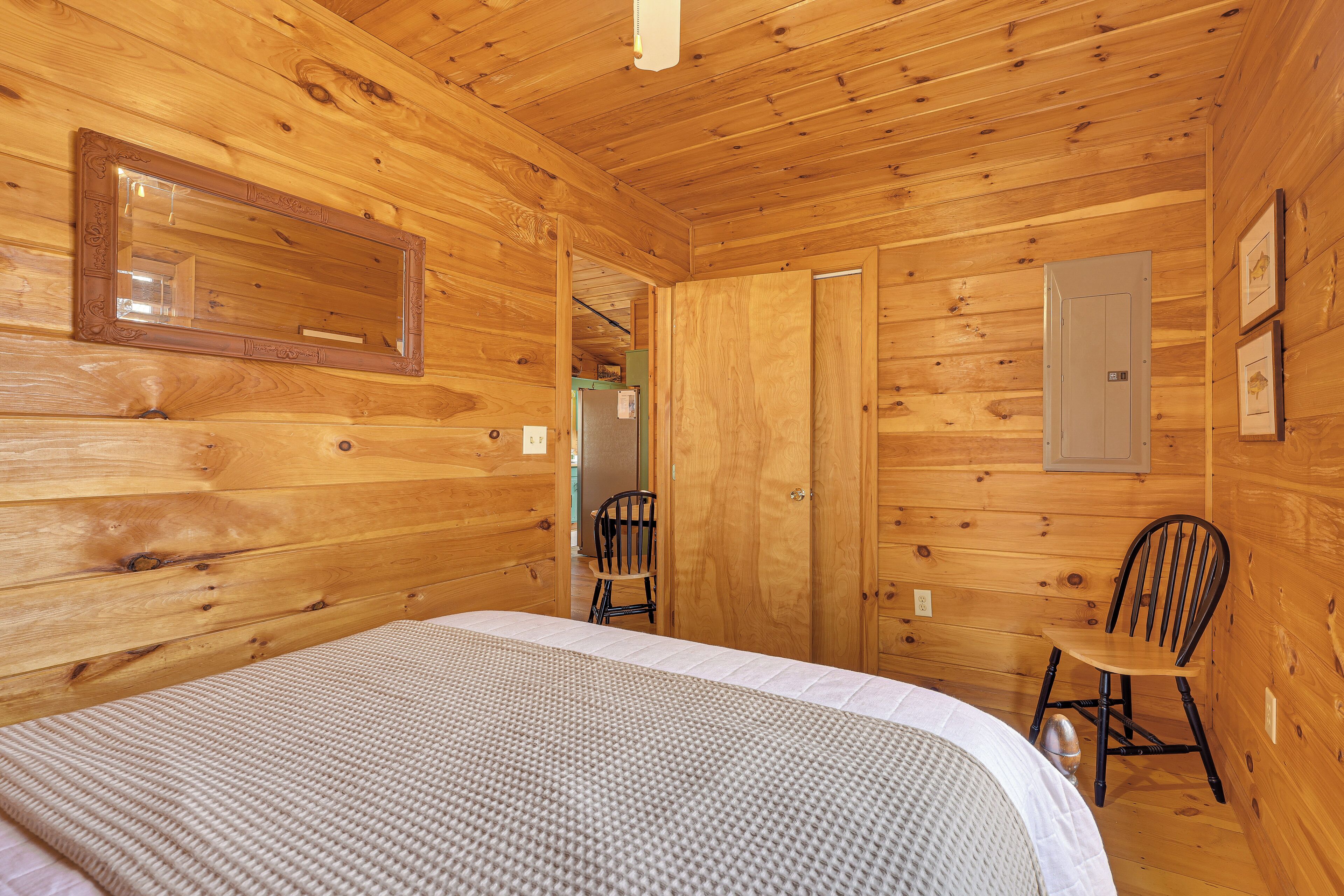 Habitación tipo cabaña de madera con una cama, una silla y una puerta que da a otra habitación.