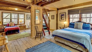 Interior rústico de una cabaña con escalera de madera, una cama grande, un escritorio y una silla.