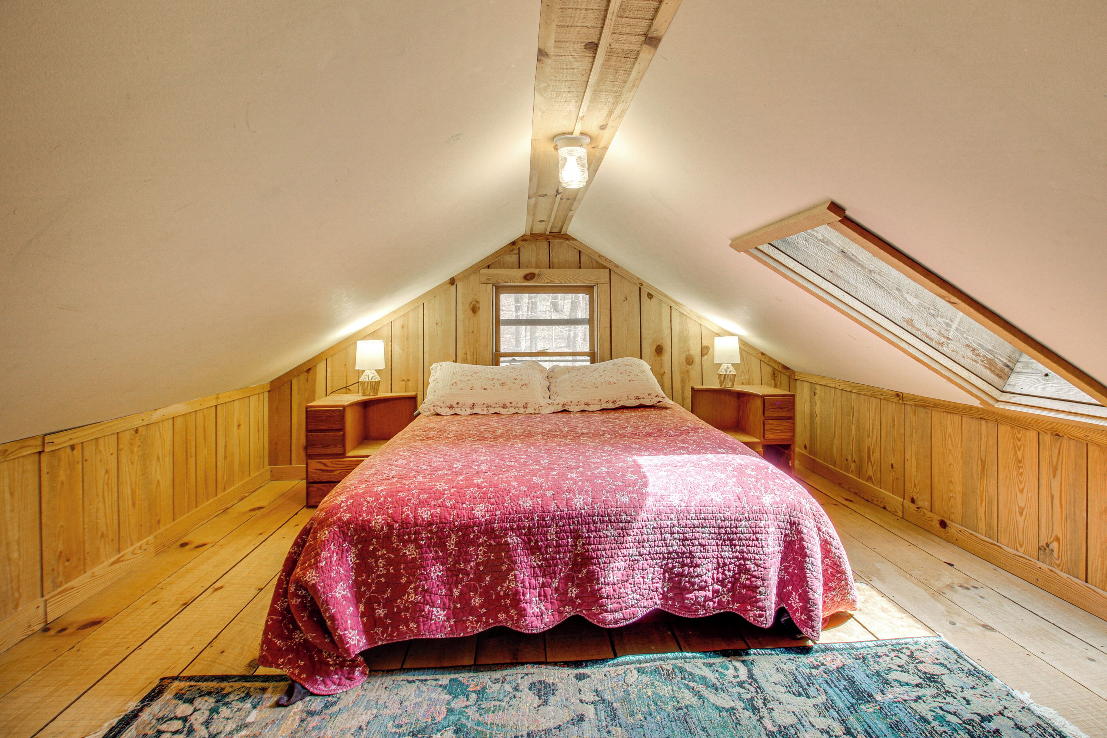 A bedroom with a sloped ceiling, wooden walls, a bed with a pink quilt, two bedside tables with lamps, and a skylight.