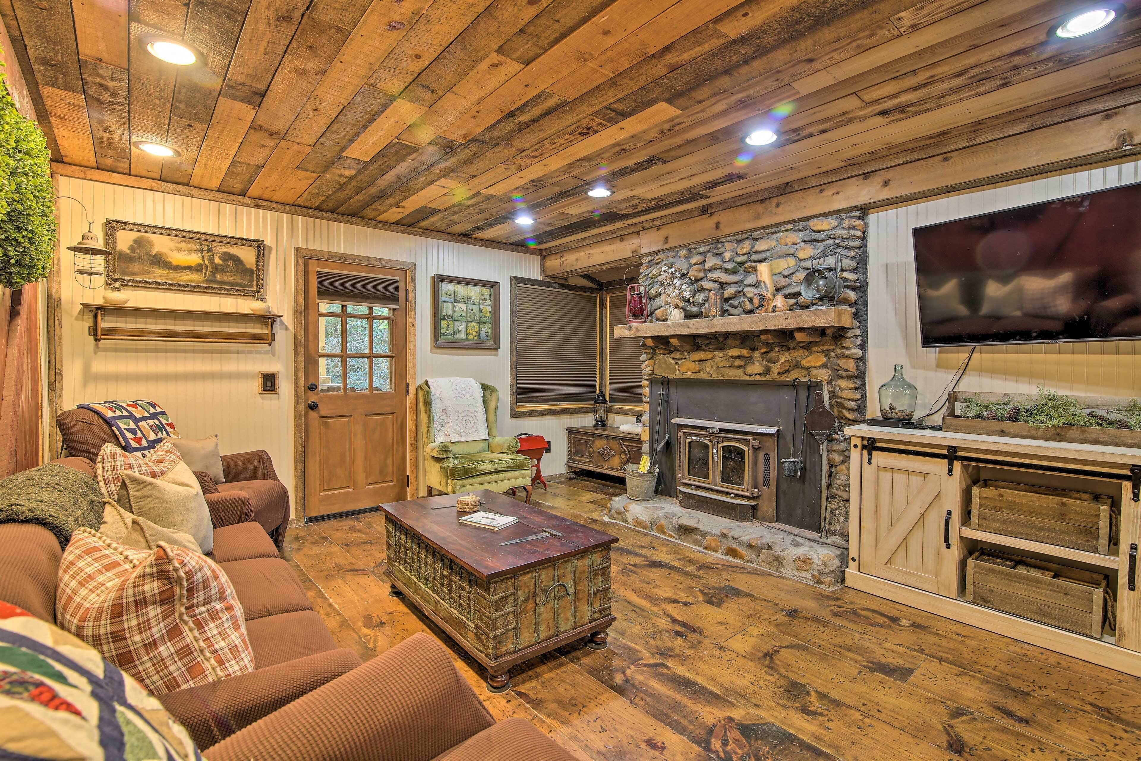 A cozy living room with a wooden ceiling, a stone fireplace, a television, and a comfortable couch.