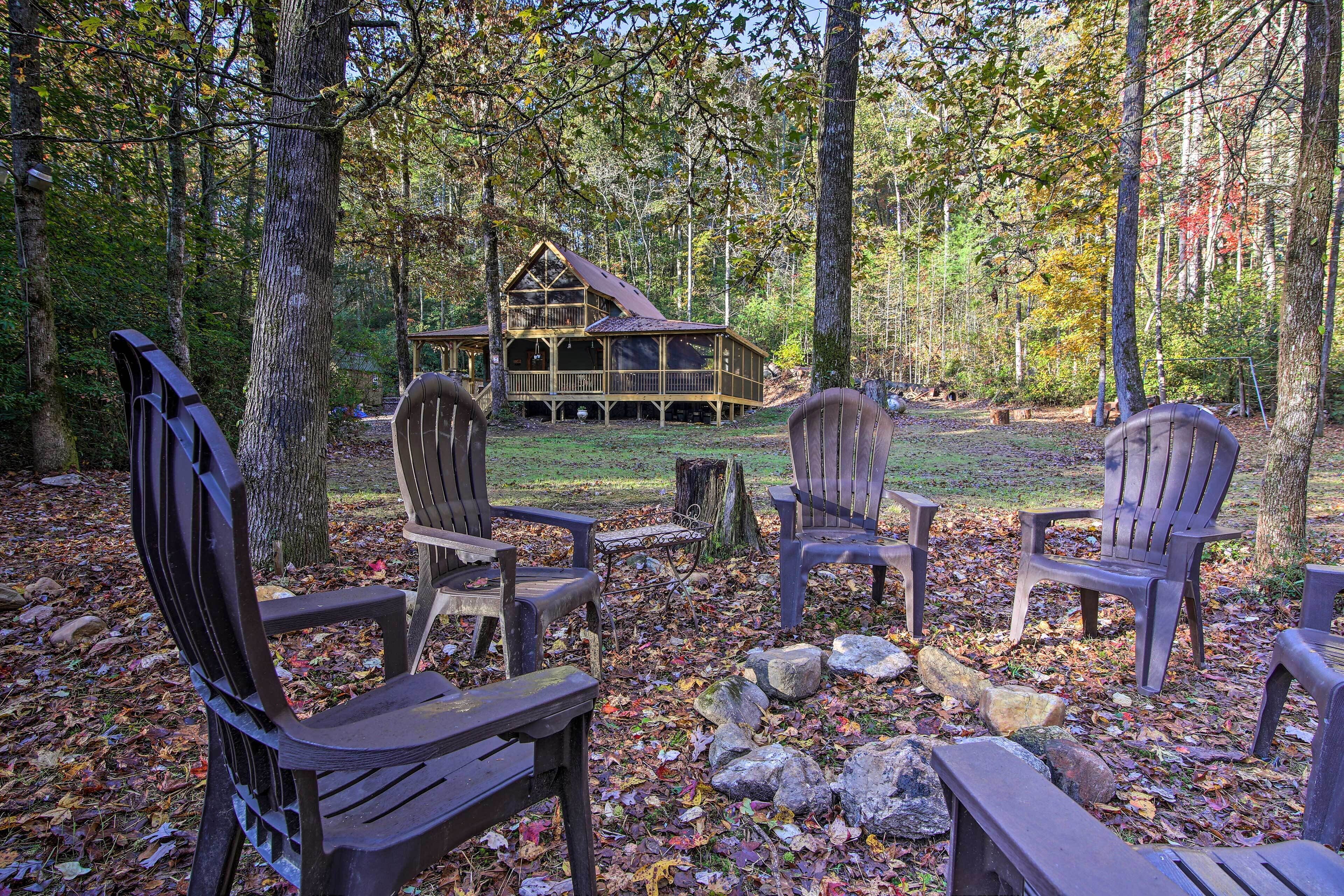 A cabin with a deck, surrounded by trees and autumn leaves, with Adirondack chairs in the foreground.