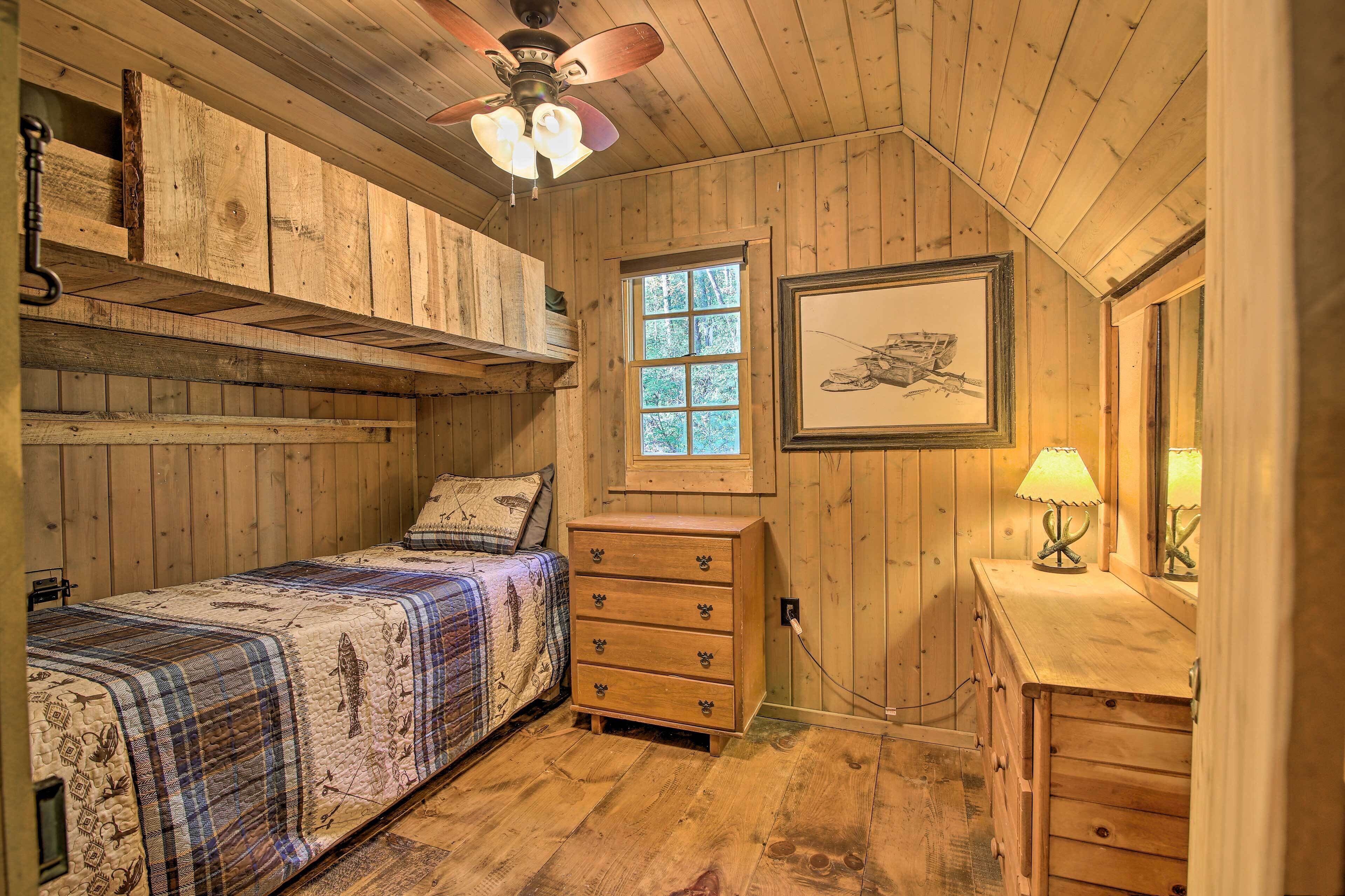 A wooden cabin bedroom with a bed, dresser, and a ceiling fan.