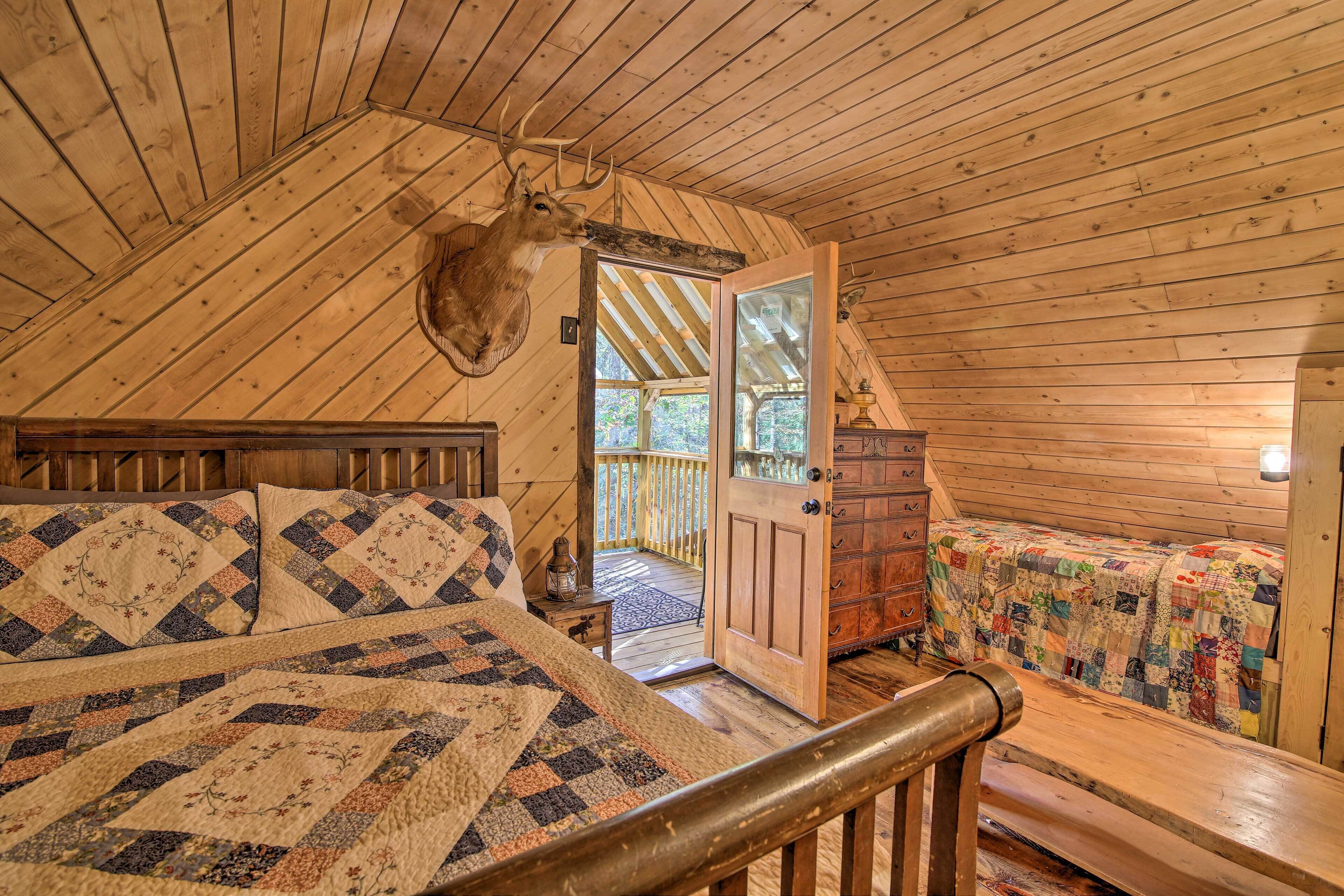 A cozy cabin bedroom with a large bed, a wooden ceiling, and a deer head mounted on the wall.