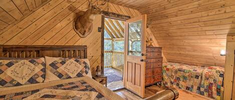 A cozy cabin bedroom with a large bed, a wooden ceiling, and a deer head mounted on the wall.