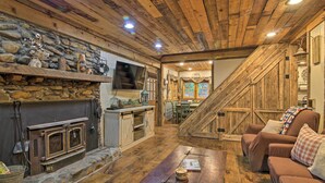 A rustic interior with a stone fireplace, wooden beams, a wooden staircase, and a cozy seating area. - Tubes & Kayaks: 5-acre North Georgia Mtn Retreat (Sautee Nacoochee)