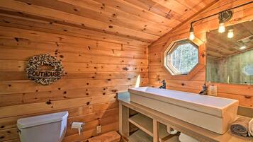 Baño de cabaña de madera con un lavamanos blanco, un inodoro y un pequeño taburete.