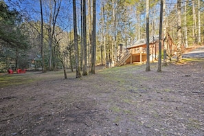A rustic cabin in a forested area with a dirt ground and a wooden staircase leading to the main entrance. - Blue Ridge Mtns Creekside Cabin w/ Hot Tub + Pier! (Blue Ridge)