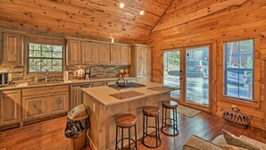 A spacious kitchen with wooden cabinets, a central island, and bar stools. - Blue Ridge Mtns Creekside Cabin w/ Hot Tub + Pier! (Blue Ridge)