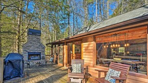 A wooden cabin with a stone fireplace, outdoor seating, and a deck overlooking a forest. - Blue Ridge Mtns Creekside Cabin w/ Hot Tub + Pier! (Blue Ridge)