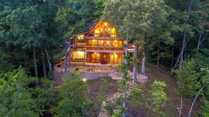 A large, multi-story log cabin surrounded by dense forest, featuring multiple balconies and a well-lit exterior. - Hot Tub + Views! Creekside Blue Ridge Mtn Escape (Mineral Bluff)