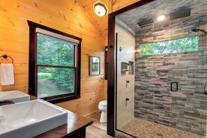 Un baño con paredes de madera, un ventanal grande, cabina de ducha con mampara de vidrio y dos lavamanos.