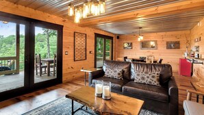 A cozy cabin interior with a leather sofa, a wooden coffee table, and a dining area. - Hot Tub + Views! Creekside Blue Ridge Mtn Escape (Mineral Bluff)