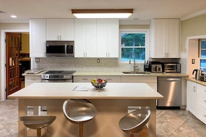 A modern kitchen with white cabinets, stainless steel appliances, a central island with stools, and a window with a view of trees. - Mcdonough Getaway w/ Private Lake on 24 Acres (McDonough)