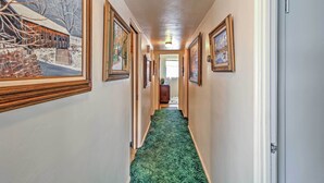 A hallway with framed artwork on the walls, a green carpet, and a door at the end.