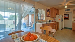 A kitchen with wooden cabinets, a dining table with a bowl of oranges, and a view of the backyard through large windows.