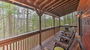 A wooden deck with a covered area, outdoor seating, and a view of a forest. - Modern Cabin w/ Deck in the Blue Ridge Mountains! (Blairsville)