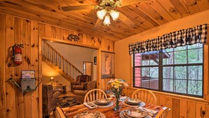 A wooden dining room with a table set for four, a vase with flowers, and a view of the outdoors through a window. - Modern Cabin w/ Deck in the Blue Ridge Mountains! (Blairsville)