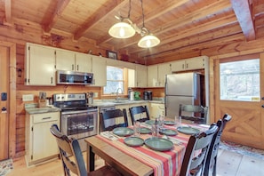 A wooden cabin kitchen with a dining table set for four, equipped with a stove, microwave, refrigerator, and ample counter space. - Waterfront Cabin w/ Beautiful River View & Hot Tub (Ellijay)