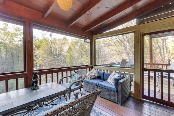 A wooden deck with wicker furniture, a sofa, and a table. - Waterfront Cabin w/ Beautiful River View & Hot Tub (Ellijay)