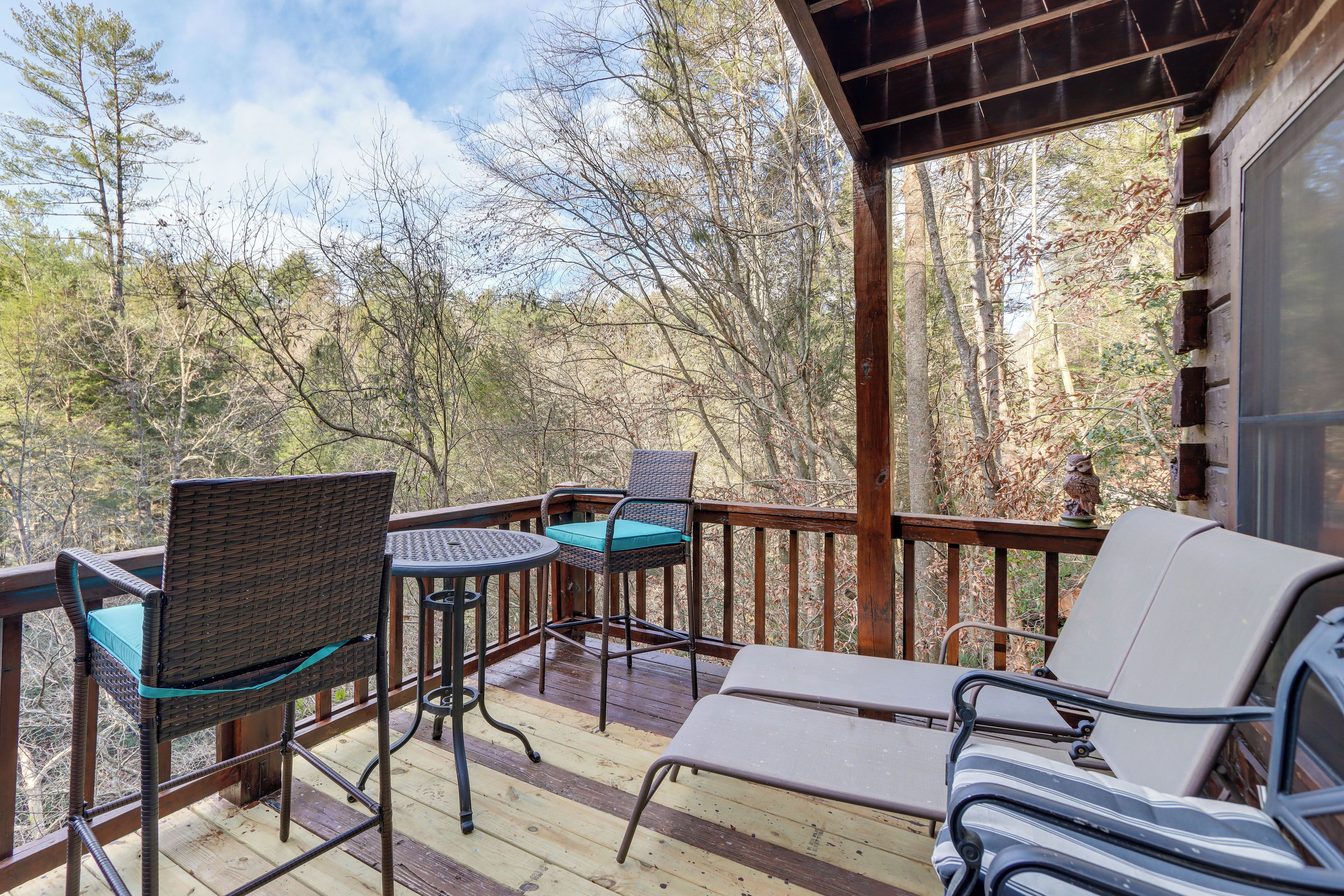 A wooden deck with wicker chairs and a table, overlooking a forested area.